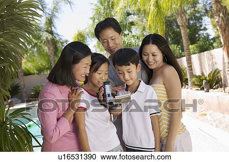 Stock Image - Family by pool in backyard Looking at Video Camera Screen, front view. Fotosearch