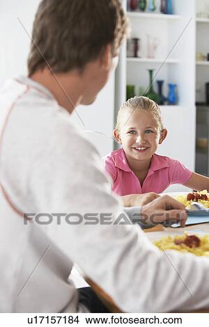 Father and daughter sitting at table eating pasta View Large Photo Image Picture - Father and daughter sitting at table eating pasta. Fotosearch