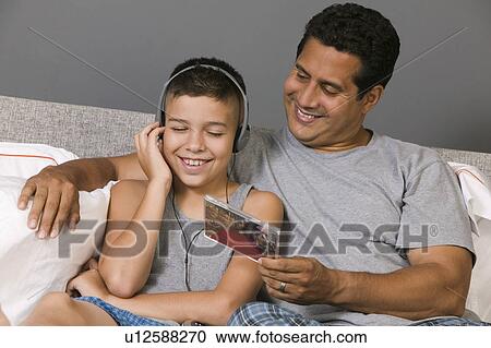 Stock Image - Father and Son listening to Music sitting on bed. Fotosearch