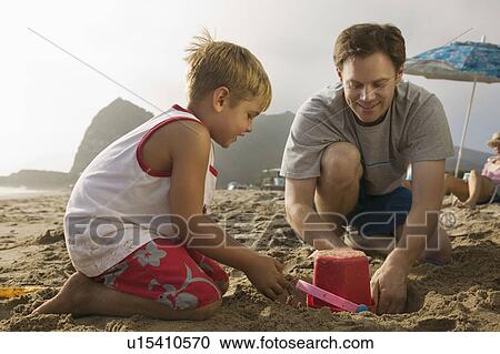 Stock Image - Father and Son Playing in Sand at Beach. Fotosearch