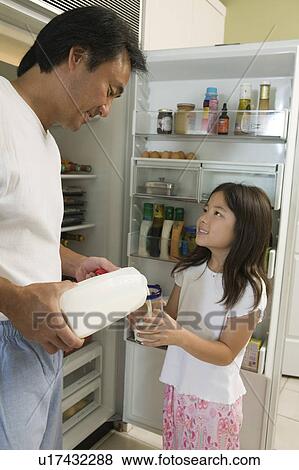 Stock Photo - Father Pouring Milk For Daughter by fridge in kitchen. Fotosearch