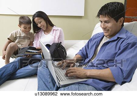 Stock Image - Father Using Laptop and mother and son Looking at DVDs on Couch. Fotosearch