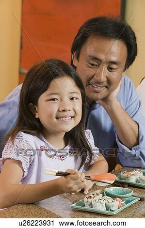 Stock Image - Father Watching Daughter Eat Sushi, portrait. Fotosearch