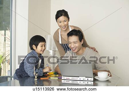 Stock Photograph - Father working on computer at dining room table, wife and son watching. Fotosearch