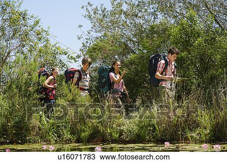 Four teenage boys and girls (16-17 years) walking by lake carrying backpack, boy reading map View Large Photo Image Stock Image - Four teenage boys and girls (16-17 years) walking by lake carrying backpack, boy reading map. Fotosearch