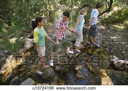 Four teenagers (16-17) crossing stream holding hands, elevated view View Large Photo Image Stock Photo - Four teenagers (16-17) crossing stream holding hands, elevated view. Fotosearch