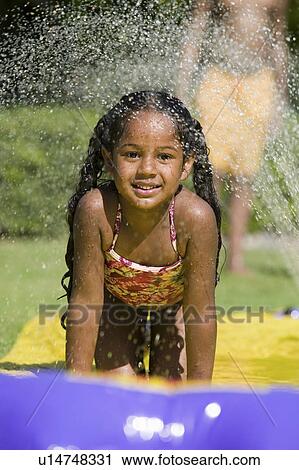 Stock Image - Girl (5-9) Sliding on water slide, portrait.. Fotosearch