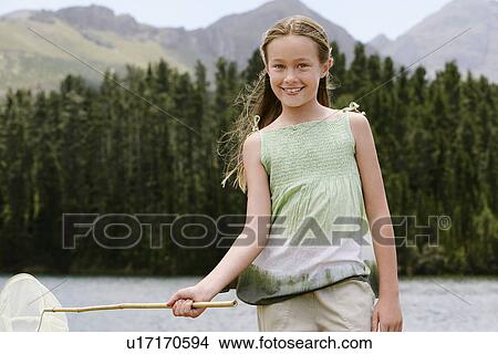 Picture - Girl (7-9) standing outdoors by lake, holding butterfly net, front view portrait.. Fotosearch