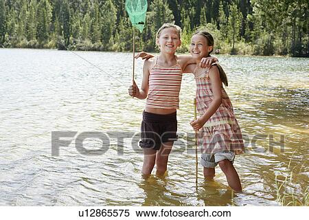 Stock Photography - Girls (7-9) standing knee-deep in lake, playing.. Fotosearch