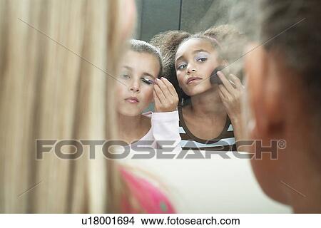 Picture - Girls looking in mirror, applying make-up and mascara. Fotosearch