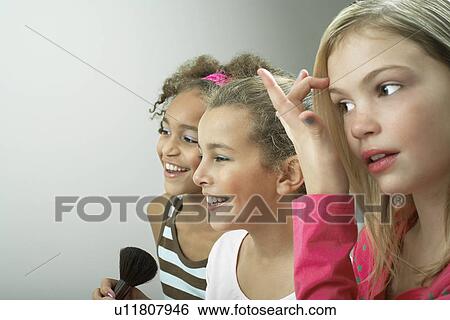 Stock Photograph - Girls standing side by side putting on make-up, fixing hair. Fotosearch