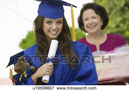 Stock Photo - Graduate holding teddy bear and diploma outside, portrait. Fotosearch