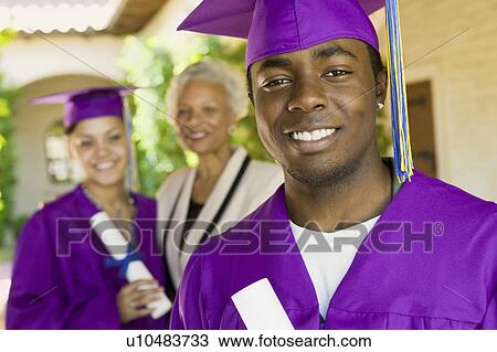 Stock Image - Graduate outside with second graduate and grandmother behind, portrait. Fotosearch