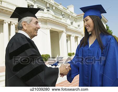 Stock Image - Graduate shaking hand of dean outside university, side view. Fotosearch