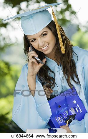 Picture - Graduate Using Cell Phone and holding gift bag outside, portrait. Fotosearch