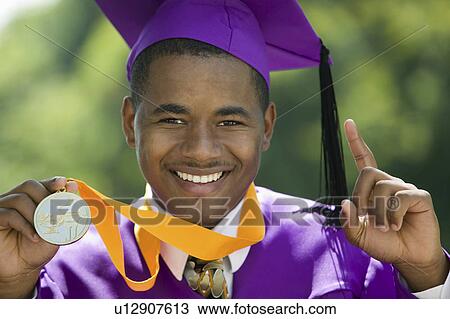 Stock Image - Graduate with medal holding one finger up outside, portrait. Fotosearch