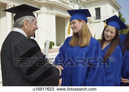 Stock Image - Graduates in line to shake hand of dean outside university, side view. Fotosearch