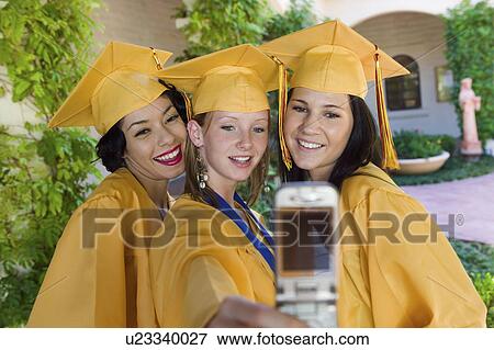 Stock Photo - Graduates taking picture with cell phone outside, front view. Fotosearch
