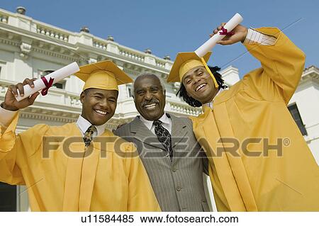 Stock Photography - Graduates with father outside university, low angle view, portrait. Fotosearch