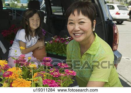 Picture - Grandmother and granddaughter loading flowers into back of SUV, portrait. Fotosearch