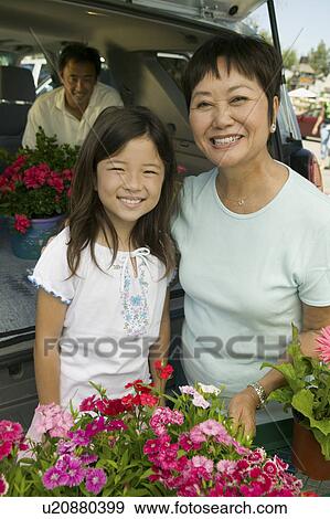 Stock Photo - Grandmother and granddaughter with flowers by back of SUV, portrait. Fotosearch