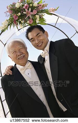 Stock Image - Groom with father under archway, outdoors, (portrait). Fotosearch