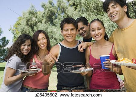 Group of young people gathered around grill at outdoor picnic. View Large Photo Image Stock Image - Group of young people gathered around grill at outdoor picnic.. Fotosearch