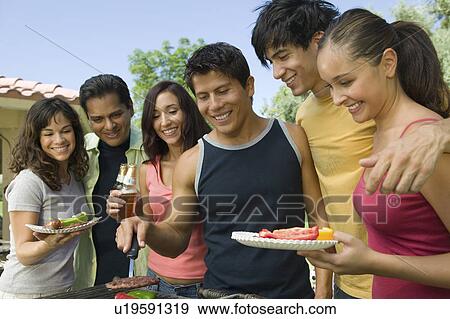 Stock Photo - Group of young people gathered around grill at outdoor picnic.. Fotosearch