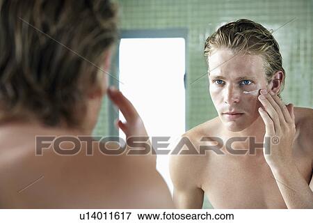 Stock Photo - Man applying facial cream in front of mirror. Fotosearch