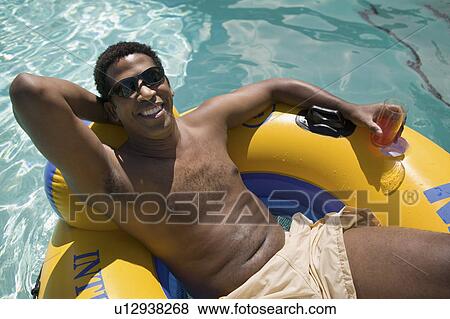 Stock Photo - Man holding drink, Relaxing on inflatable raft in swimming pool, elevated view portrait.. Fotosearch