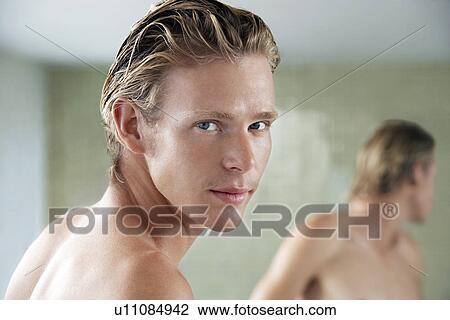 Stock Image - Man in bathroom, looking over shoulder, portrait. Fotosearch