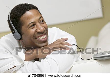 Stock Image - Man lying on sofa Listening to Music on portable CD player, close up, front view. Fotosearch