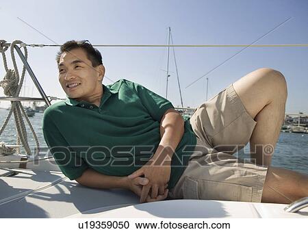 Stock Image - Man relaxing on sailboat. Fotosearch