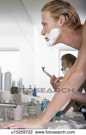 Stock Image - Man shaving face in bathroom. Fotosearch