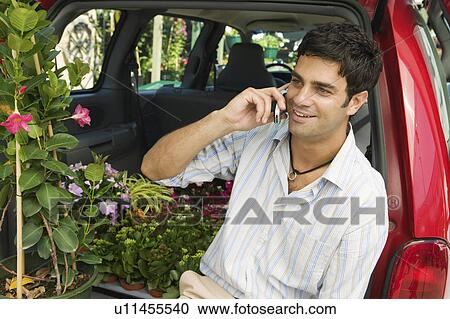 Man sitting by flowers on back of minivan using cell phone View Large Photo Image Stock Image - Man sitting by flowers on back of minivan using cell phone. Fotosearch