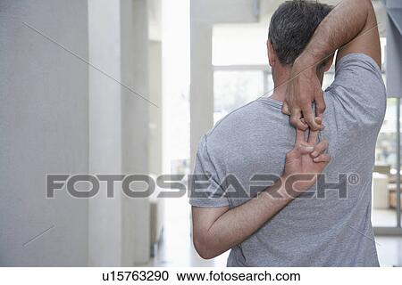 Stock Image - Man standing, stretching arms behind back, back view. Fotosearch