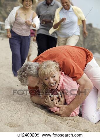 Stock Photography - Man tackling woman with football on beach. Fotosearch
