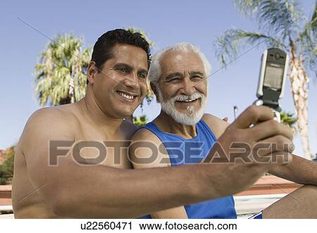 Stock Image - Man using mobile phone, photographing self with senior father.. Fotosearch