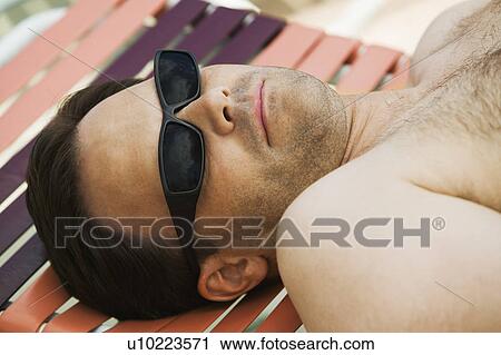 Stock Image - Man wearing sunglasses, lying on sunlounger.. Fotosearch