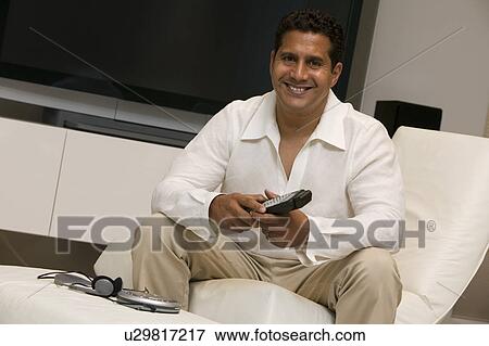 Stock Photo - Man with remote control sitting in front of Large Screen TV in living room, portrait. Fotosearch