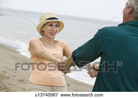 Stock Photo - Mature couple holding hands on beach. Fotosearch