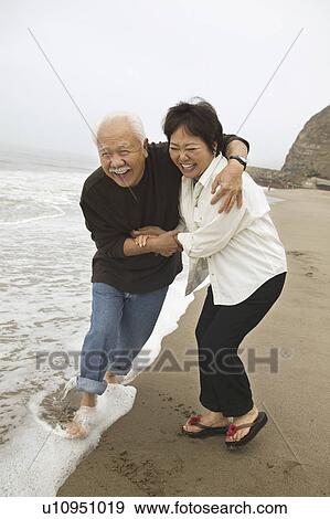 Stock Photo - Mature couple playing in surf on beach. Fotosearch