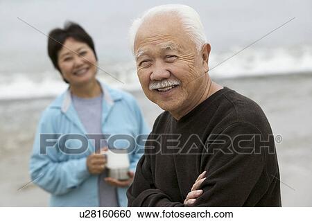 Stock Image - Mature man and wife at beach, (portrait). Fotosearch