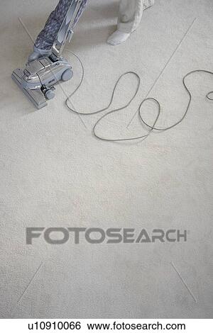 Stock Photograph - Mature woman vacuuming carpet, low section. Fotosearch