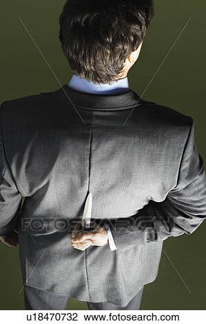 Mid-adult businessman standing, holding knife behind back, back view View Large Photo Image Stock Image - Mid-adult businessman standing, holding knife behind back, back view. Fotosearch