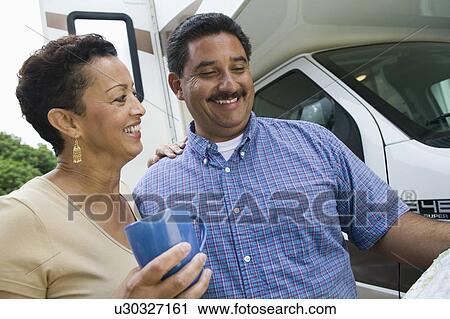 Stock Image - Mid-adult couple standing beside caravan. Fotosearch