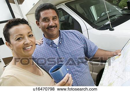 Stock Photo - Mid-adult couple standing beside caravan and looking at camera. Fotosearch