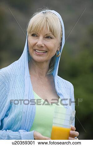 Stock Image - Mid-adult woman holding a glass of orange juice. Fotosearch