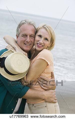 Middle-aged couple embracing on beach and looking at camera View Large Photo Image Stock Image - Middle-aged couple embracing on beach and looking at camera. Fotosearch