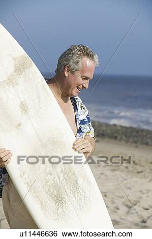 Stock Photograph - Middle-aged man holding a surfboard. Fotosearch
